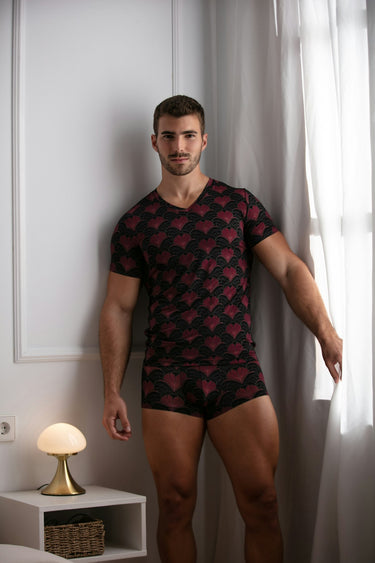 Man wearing a black patterned shirt and matching underwear in a room with white walls and a small table.